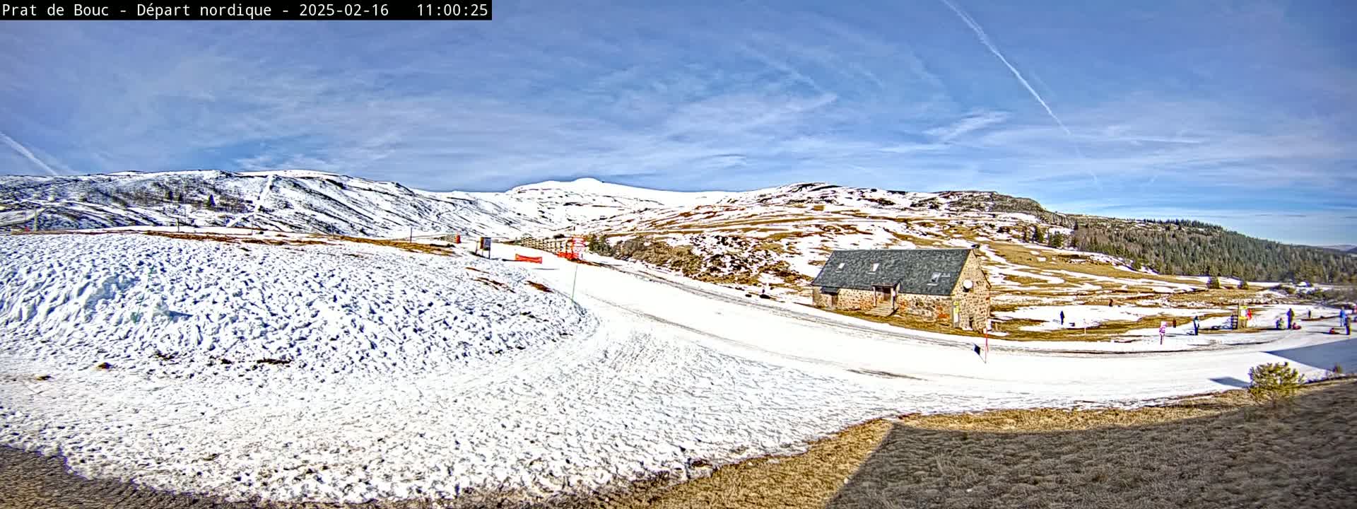A snow-covered landscape with a small stone building, under a mostly sunny sky, features a gently sloping path winding through the snow.