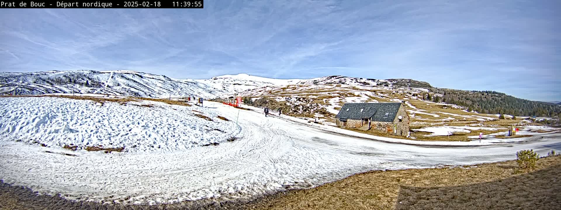 A snow-covered landscape with a small stone building, under a mostly sunny sky.