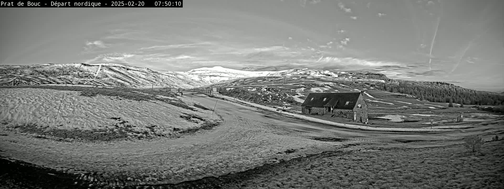 A snow-dusted landscape with a lone stone building near a winding road, under a partly cloudy sky.