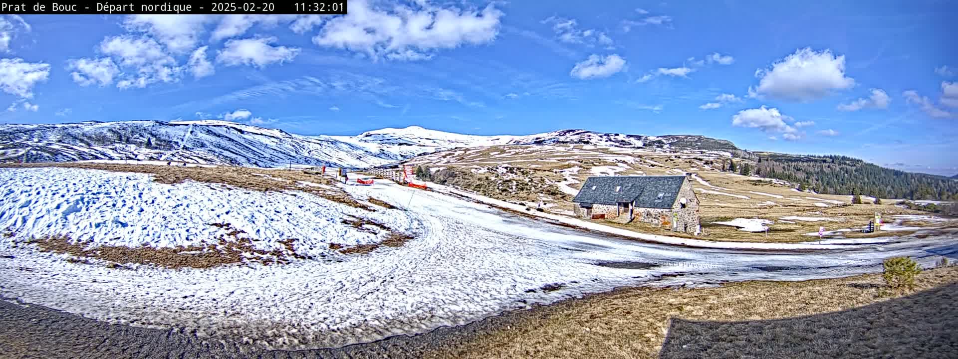 A snow-dusted landscape with a small stone building and a partly sunny sky.