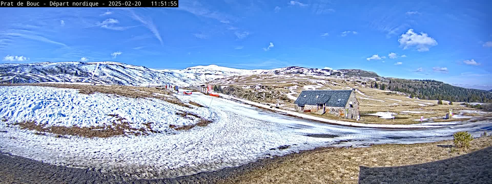 A snow-covered landscape with a stone building, under a mostly sunny sky with a few clouds.