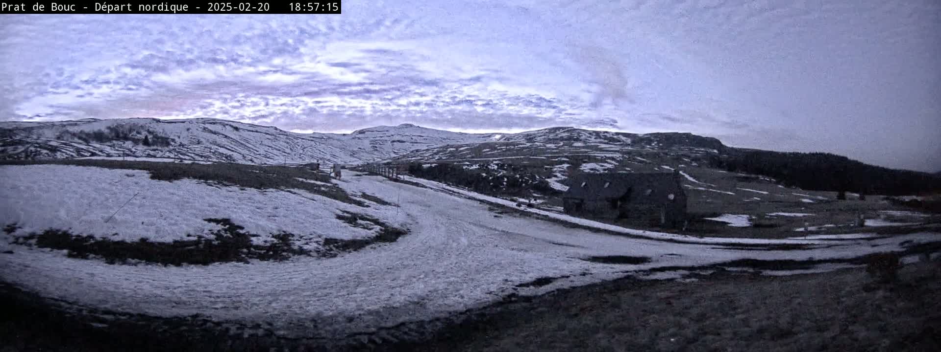 A snow-covered landscape with a building and a winding path under a cloudy, twilight sky.