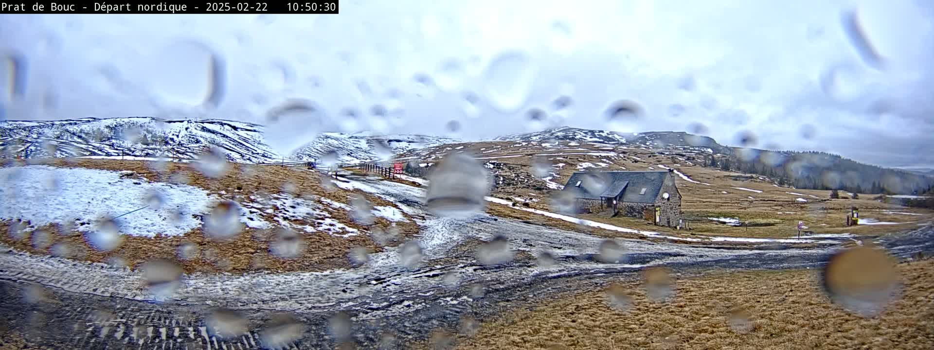 A rain-covered view shows a stone building on a snow-dusted, hilly landscape.