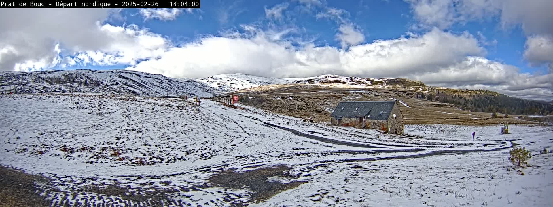 A stone building sits on a snow-covered hillside under a partly cloudy sky.