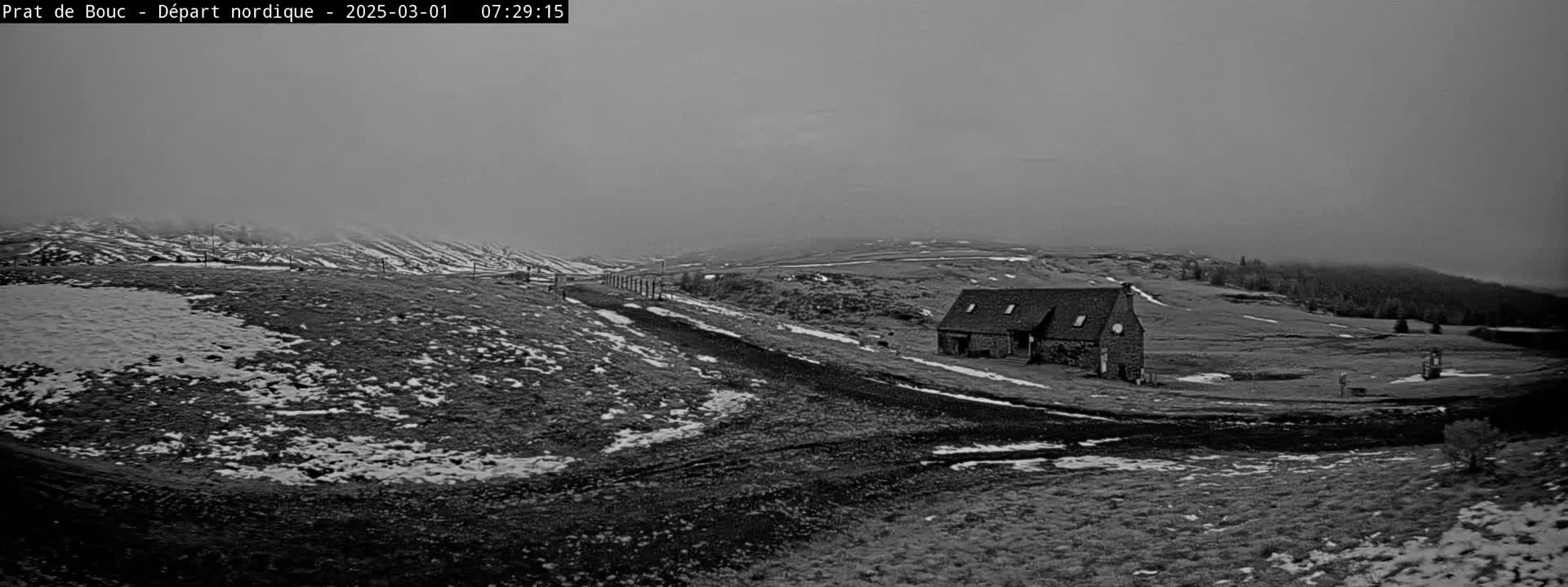 A stone building sits on a snow-dusted hillside under a hazy, overcast sky.