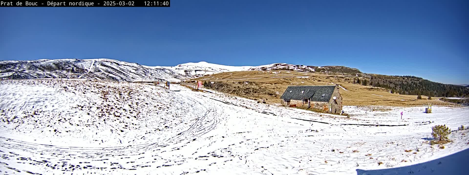 A snow-covered landscape with a stone building and distant mountains under a clear blue sky.
