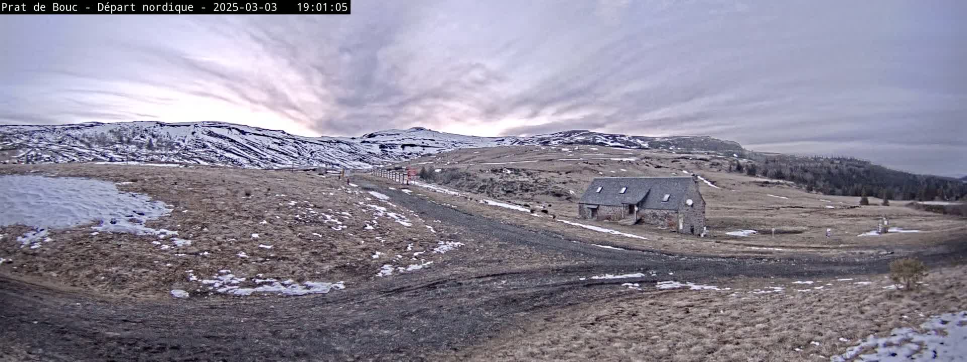 A stone building sits on a snow-dusted, hilly landscape under a cloudy sky with a hint of sunset.