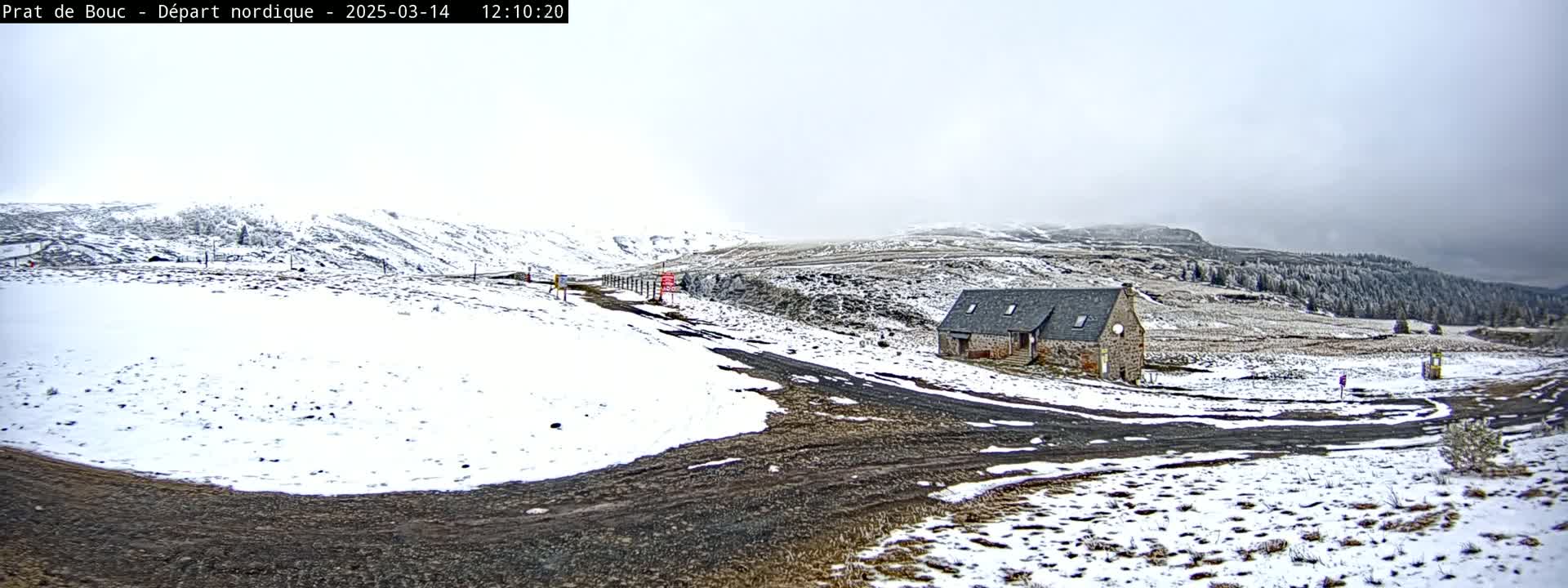 A snow-covered landscape with a small stone building and a dirt road under an overcast sky.