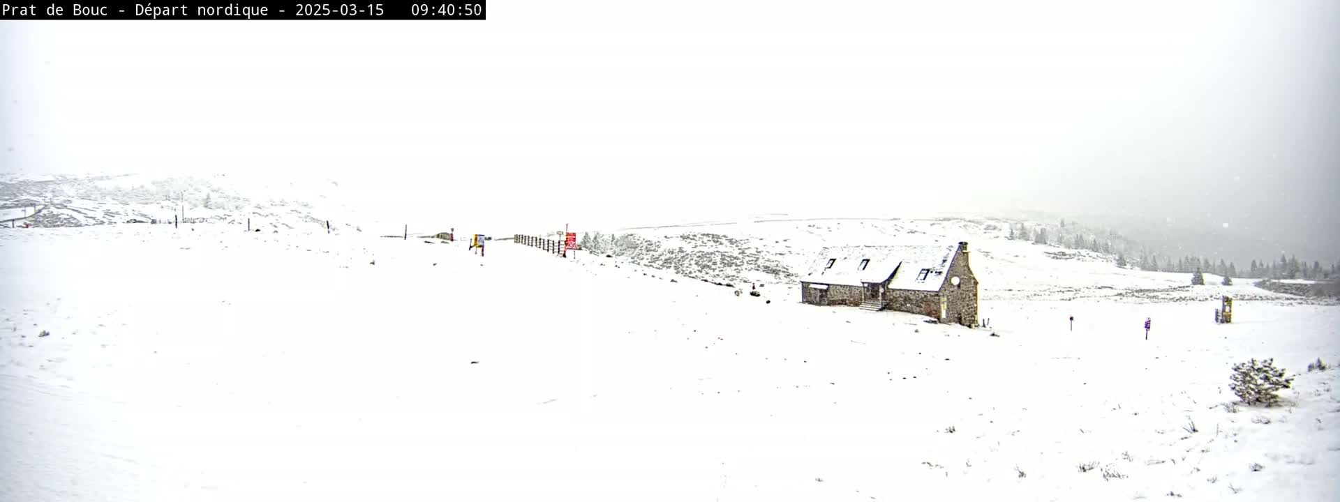 A snow-covered landscape with a stone building is seen under heavy snowfall.
