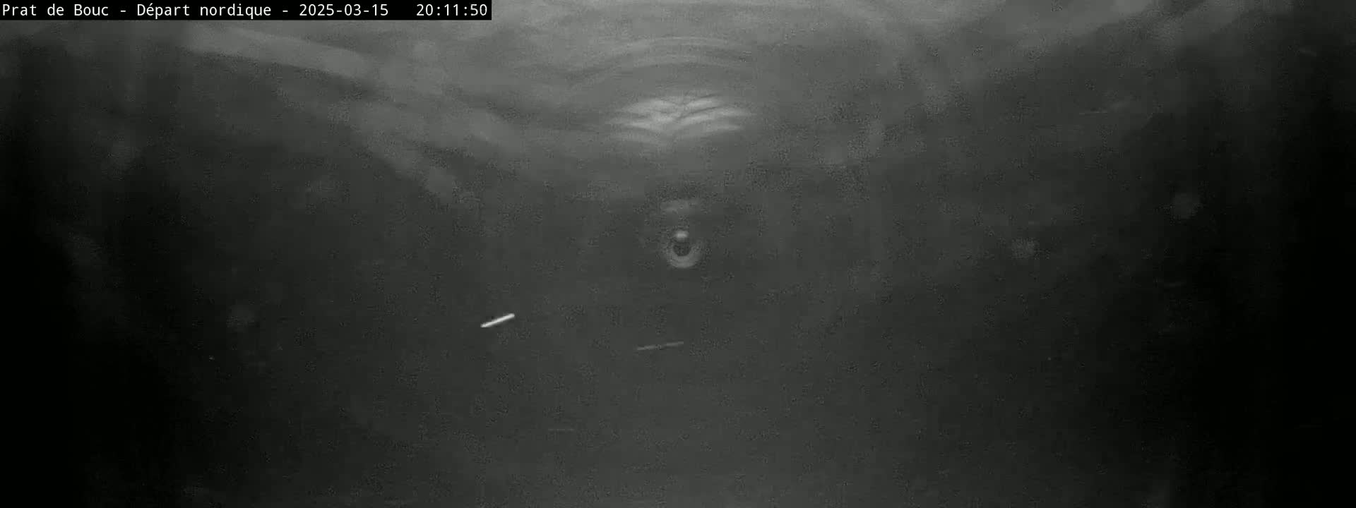A grainy, low-light image shows a dark, possibly underground, space with a vaguely discernible shape in the center.