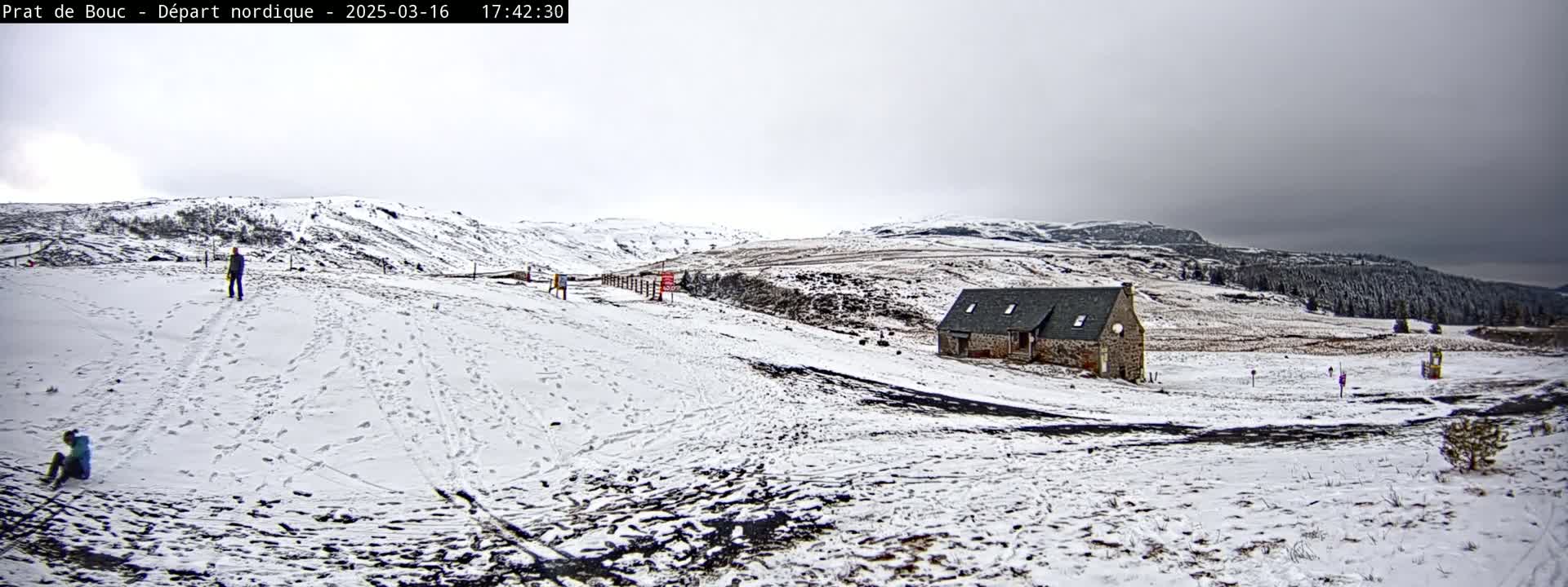 A snow-covered landscape with a small stone building and a few people, under an overcast sky.