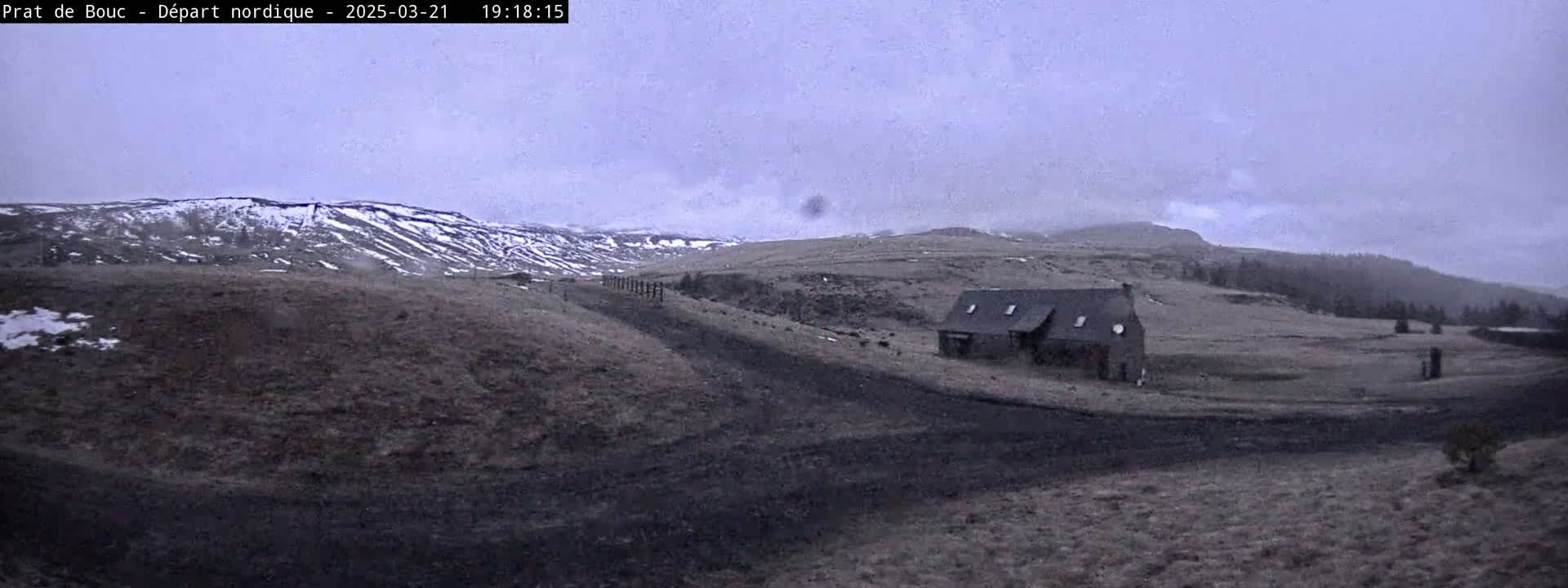 A dark gray building sits in a desolate, snow-dusted landscape under an overcast sky.