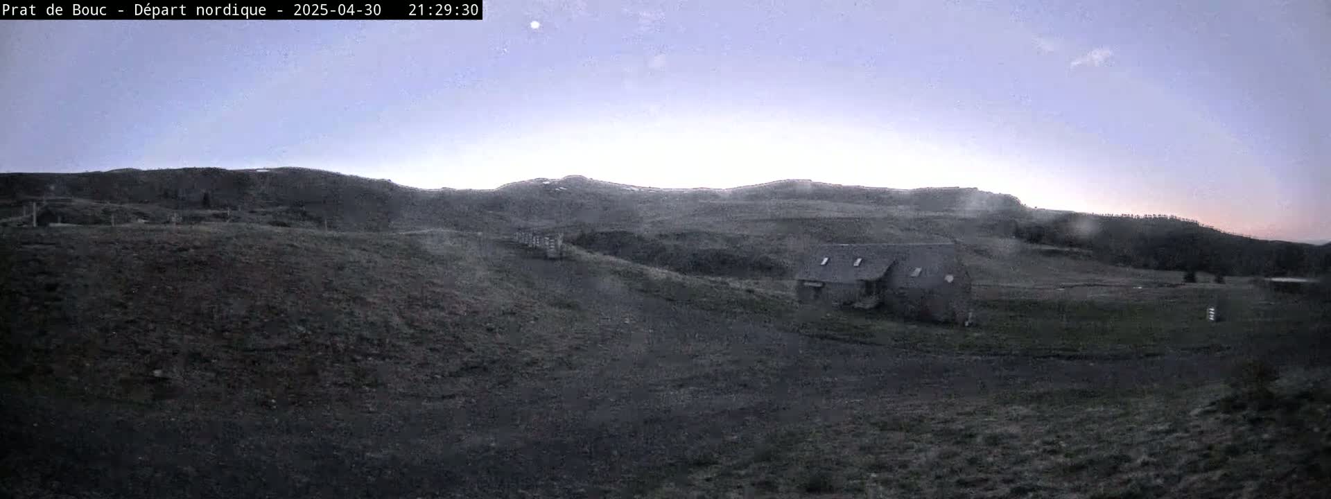 A small building sits on a dark, sparsely vegetated hillside under a twilight sky.