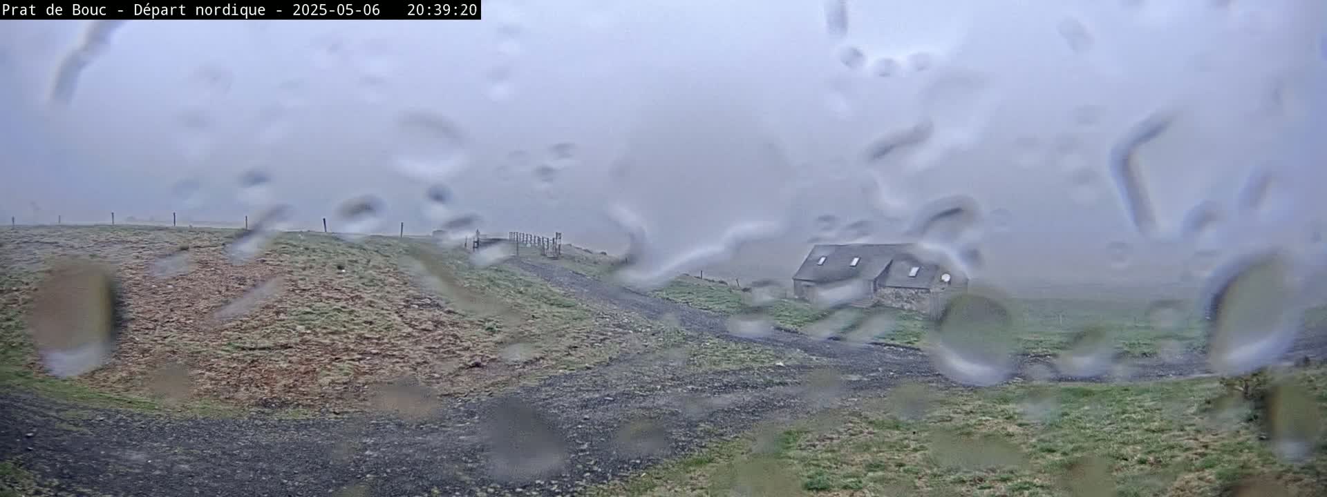 A small stone building is visible through rain-covered glass on a sparsely vegetated hilltop.