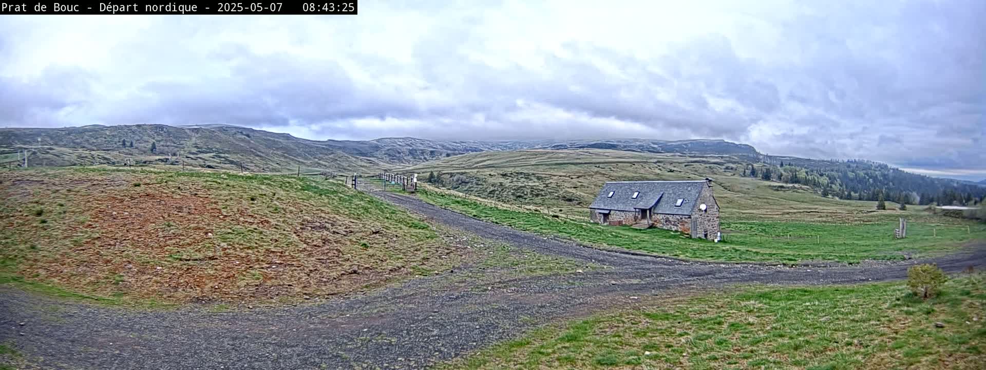 A gravel road leads to a stone building in a grassy valley under a cloudy sky.