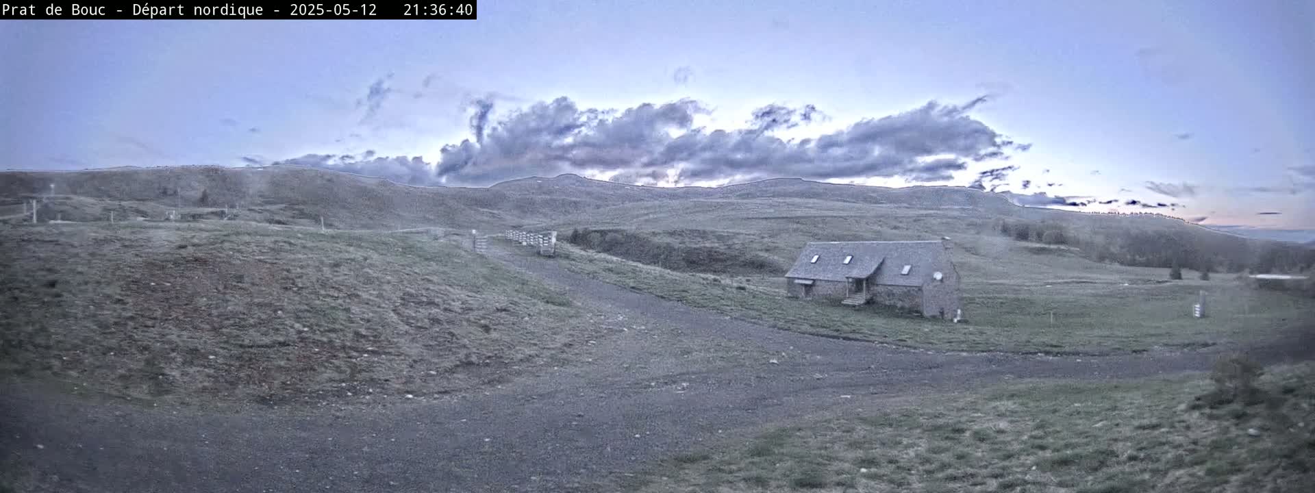 A low stone building sits on a grassy hillside under a partly cloudy twilight sky.
