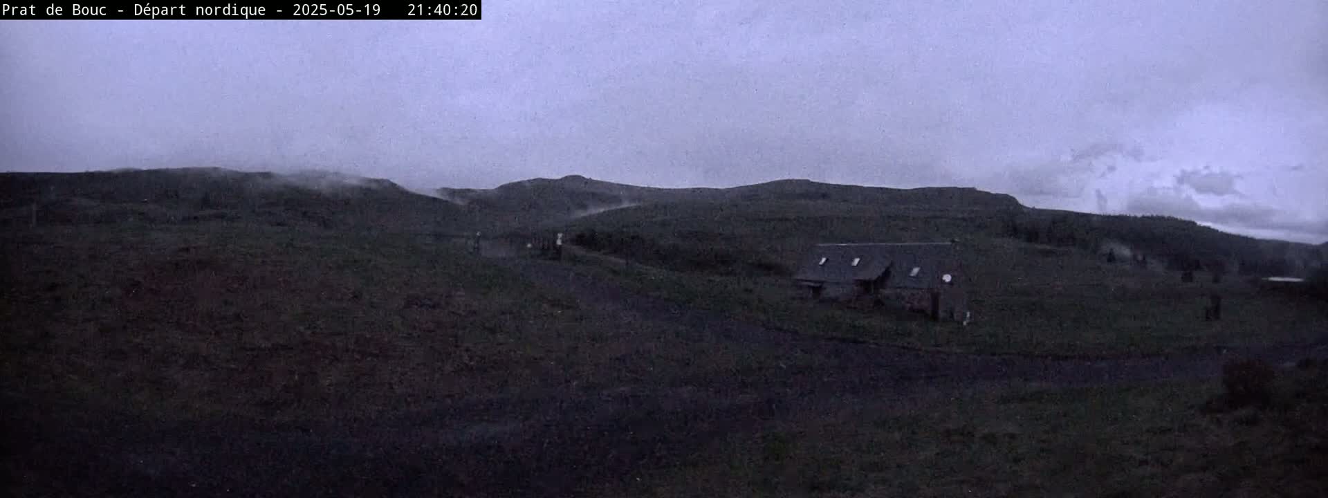 A small house sits on a dark, grassy hillside under an overcast, dusky sky.
