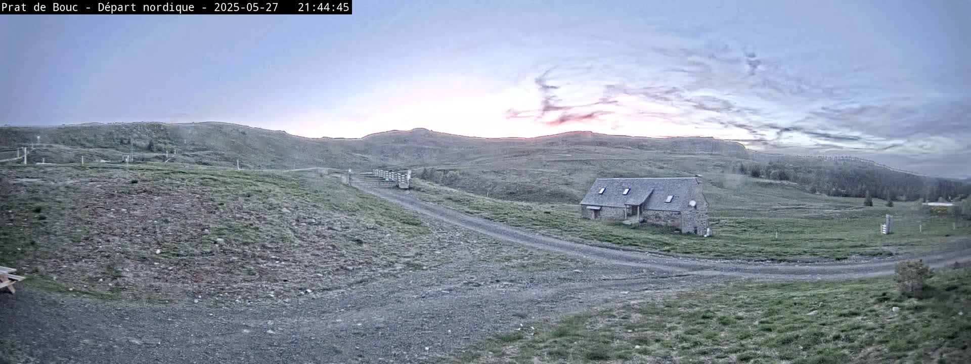 A low stone building sits on a grassy hillside under a partly cloudy, twilight sky.