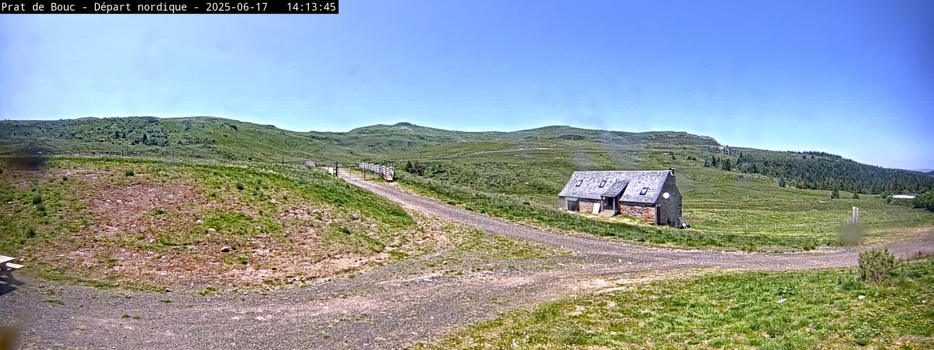 A gravel road leads to a stone building in a grassy field under a clear blue sky.