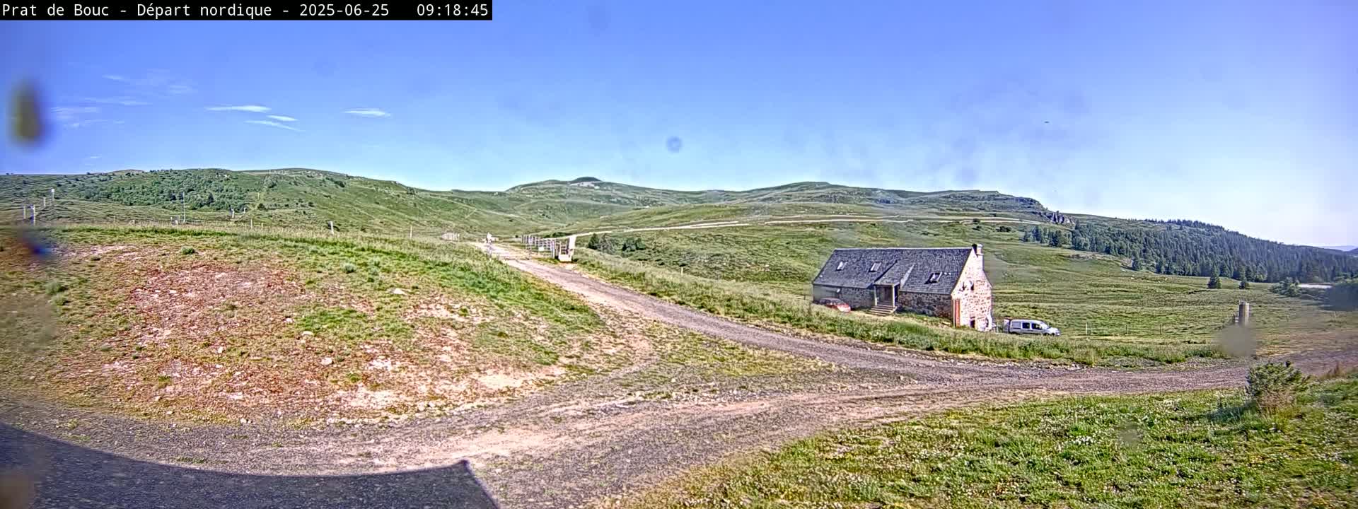 A stone house sits on a grassy hillside with a dirt road leading to it under a clear blue sky.