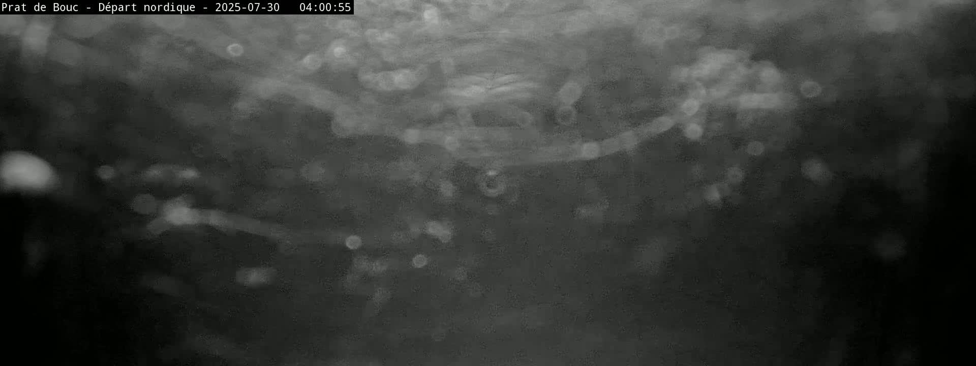 A blurry, dark gray image shows indistinct shapes and light spots, possibly depicting nighttime or low-light conditions with some precipitation.