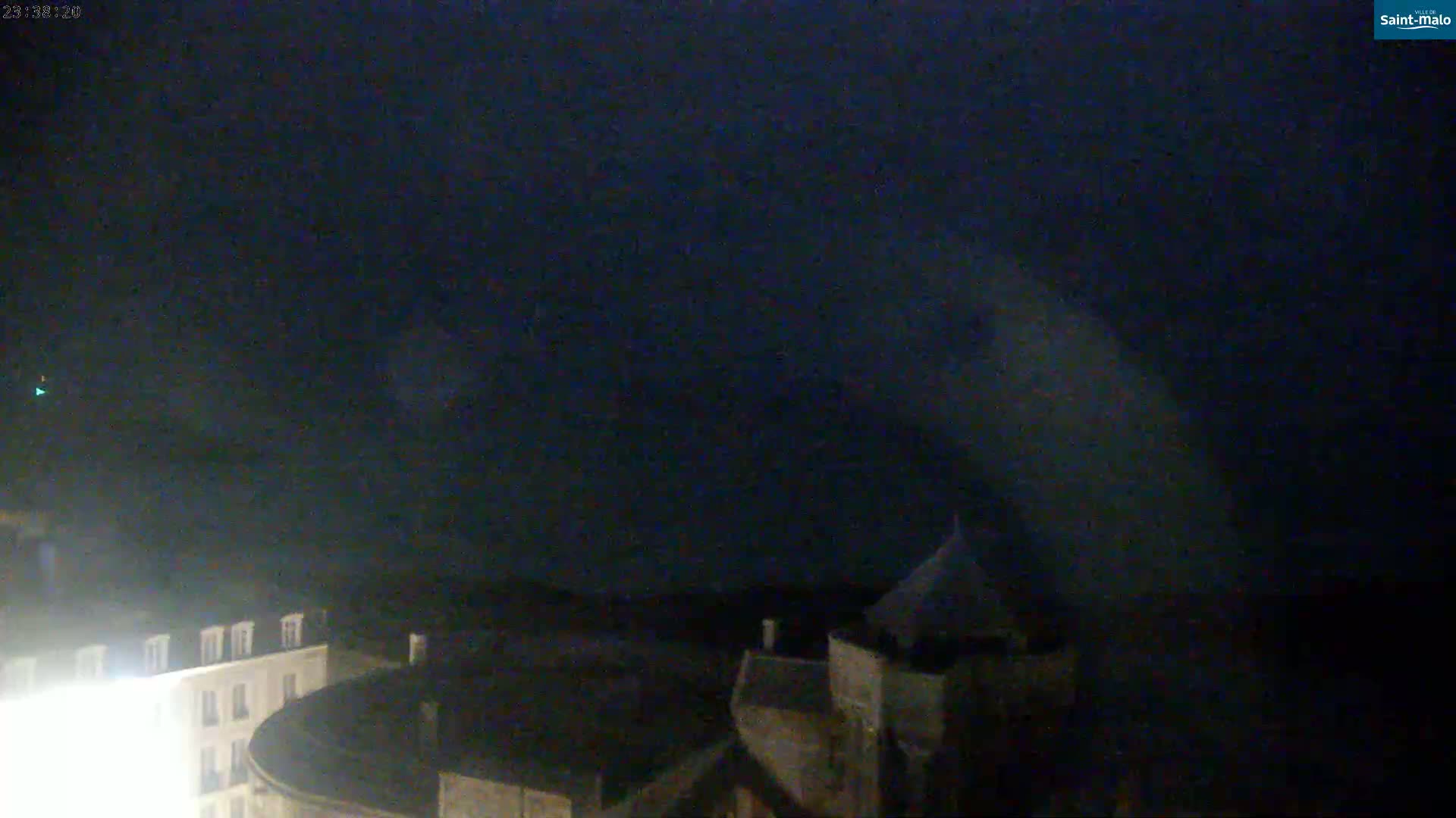A dark, nighttime scene shows the tops of buildings under a mostly clear, dark sky.
