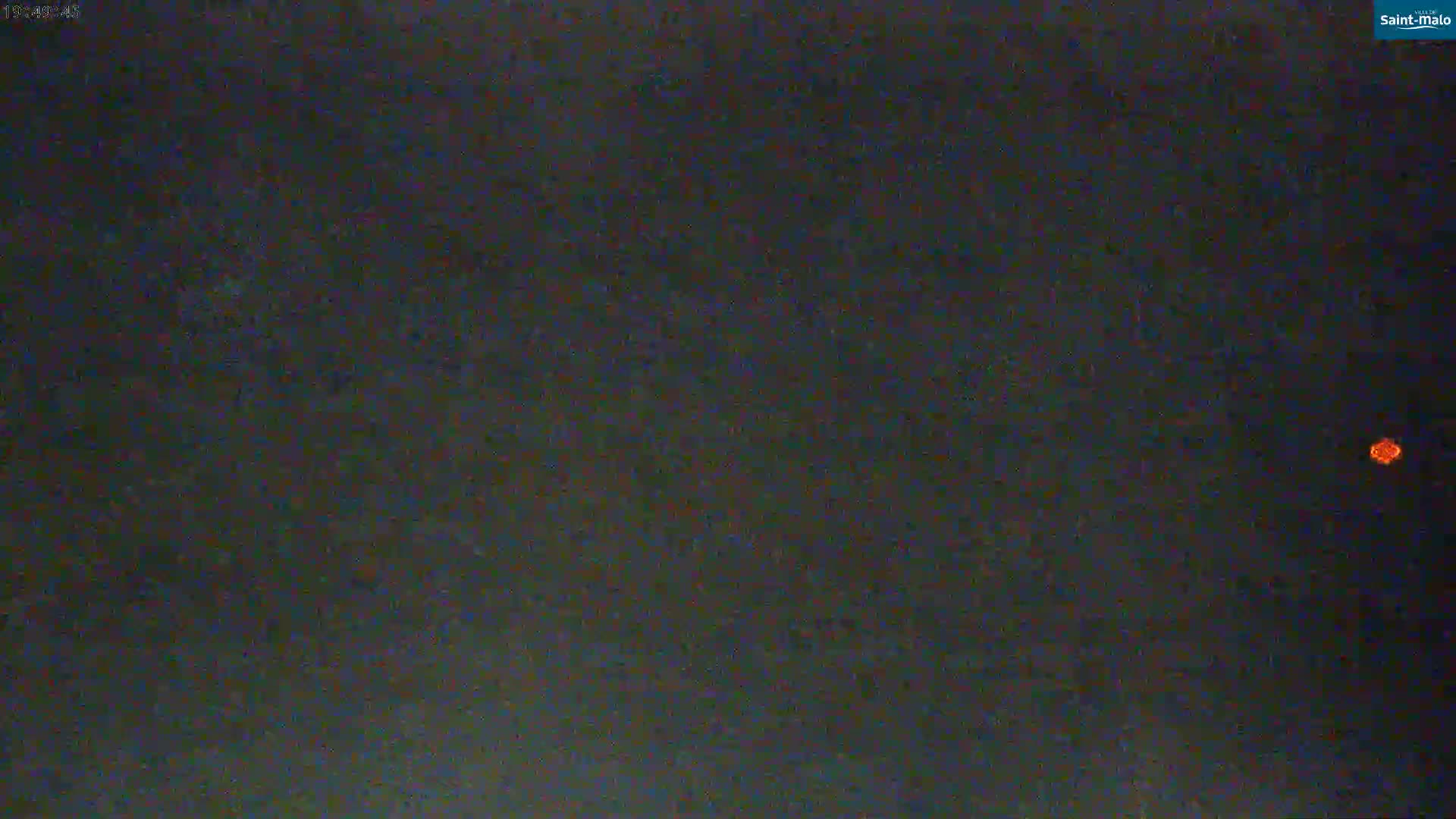 A small, orange light is visible in a dark, nighttime sky.