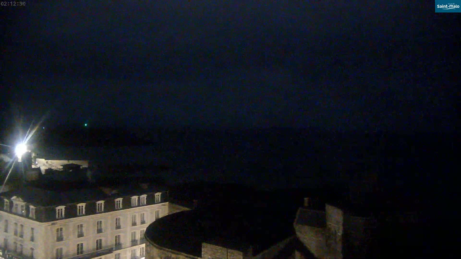 A nighttime, low-light view shows a section of a city near a dark body of water under a clear, dark sky.