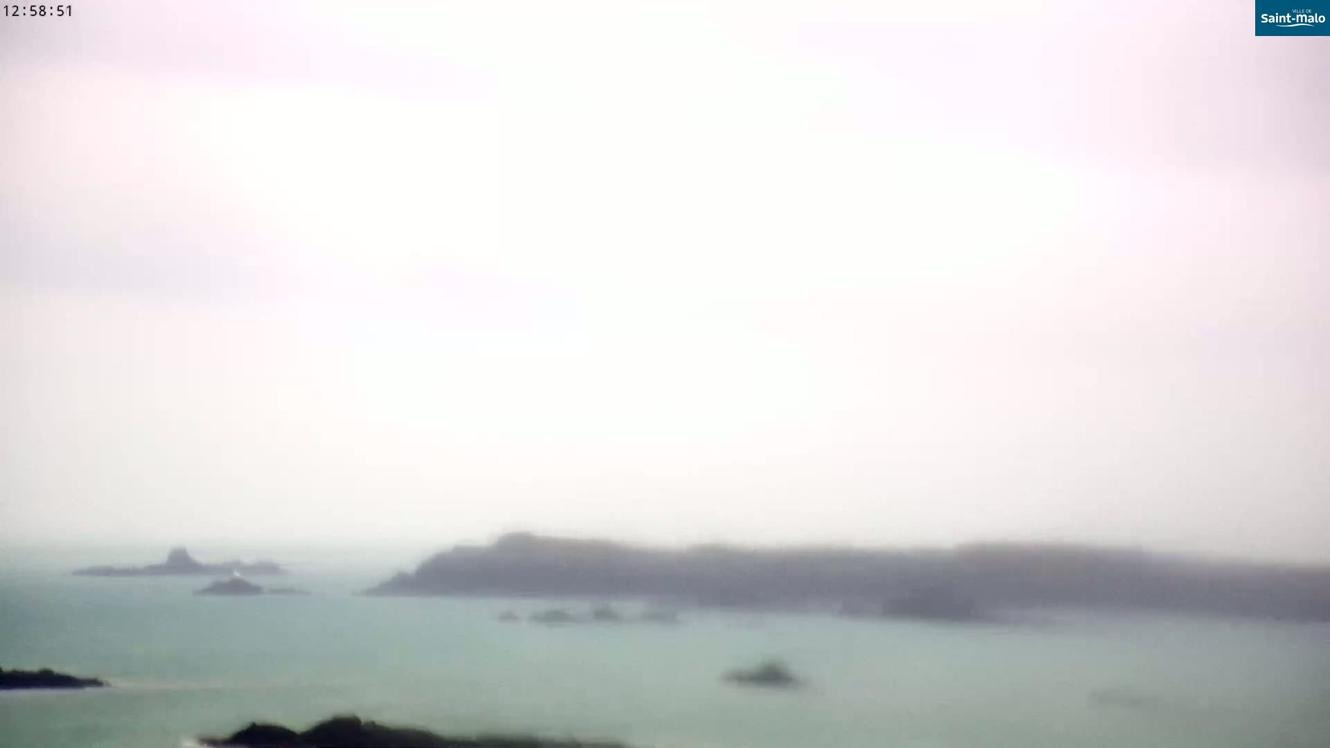A hazy, overcast day reveals a distant view of several small, dark islands in a calm body of water.