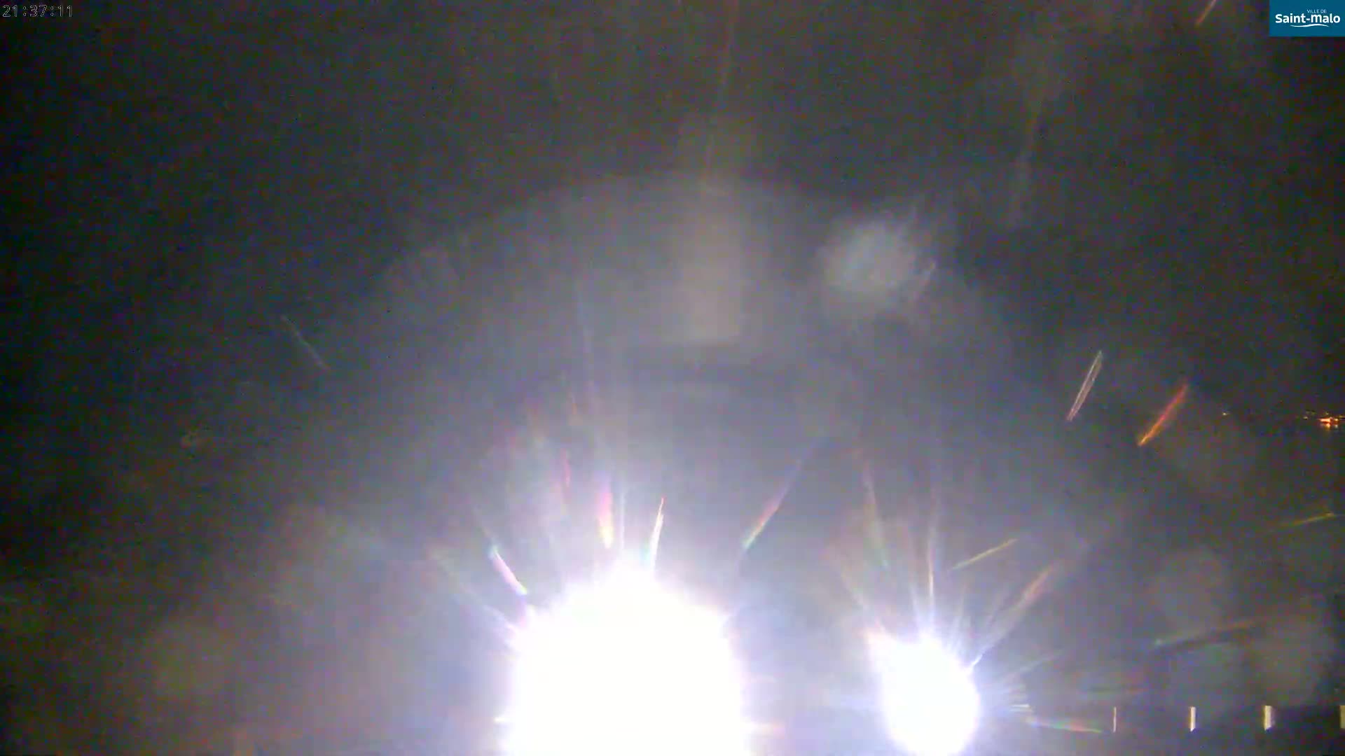 Two bright lights with radiating streaks of light are visible at night, possibly from headlights.