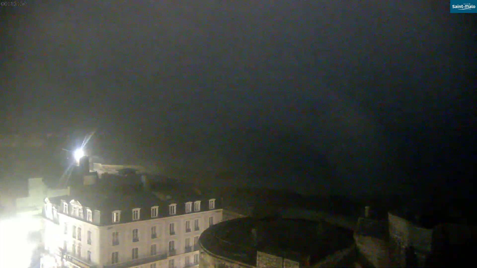 A nighttime view of a city shows a multi-story building under a dark, foggy sky.