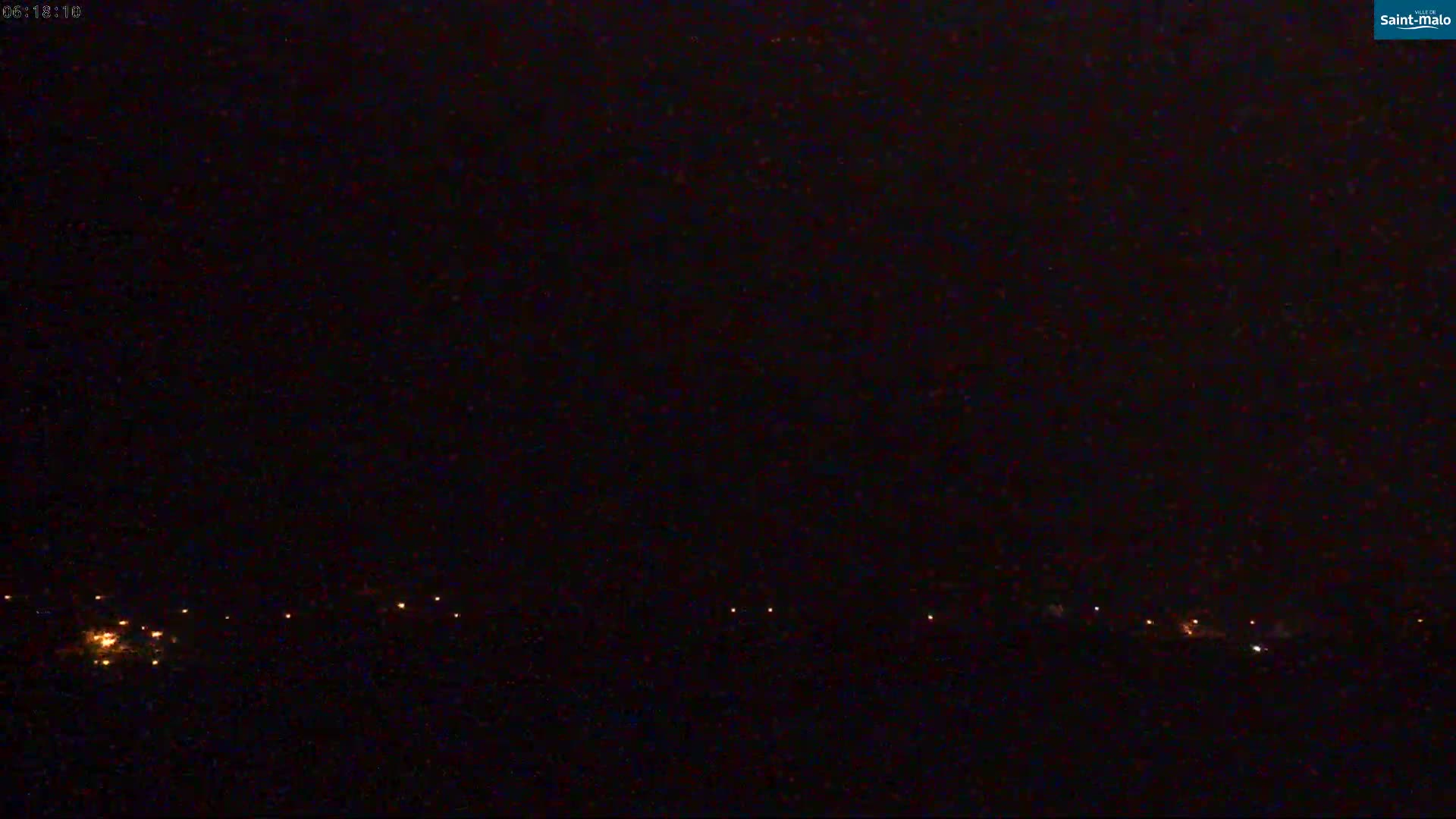 A nighttime, dark image shows a line of distant lights on a dark horizon under a mostly clear sky.