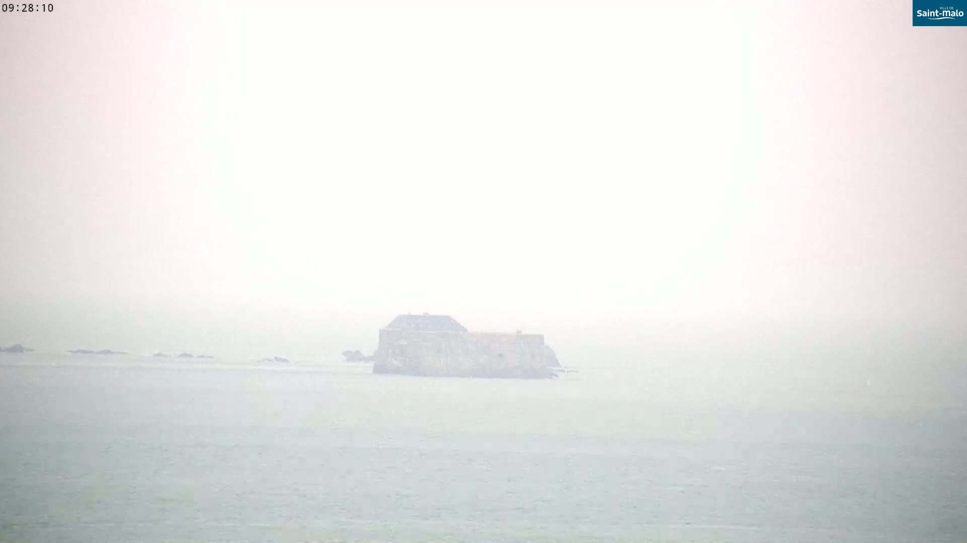 A hazy, distant view of a stone fort situated on a small island in a calm sea.