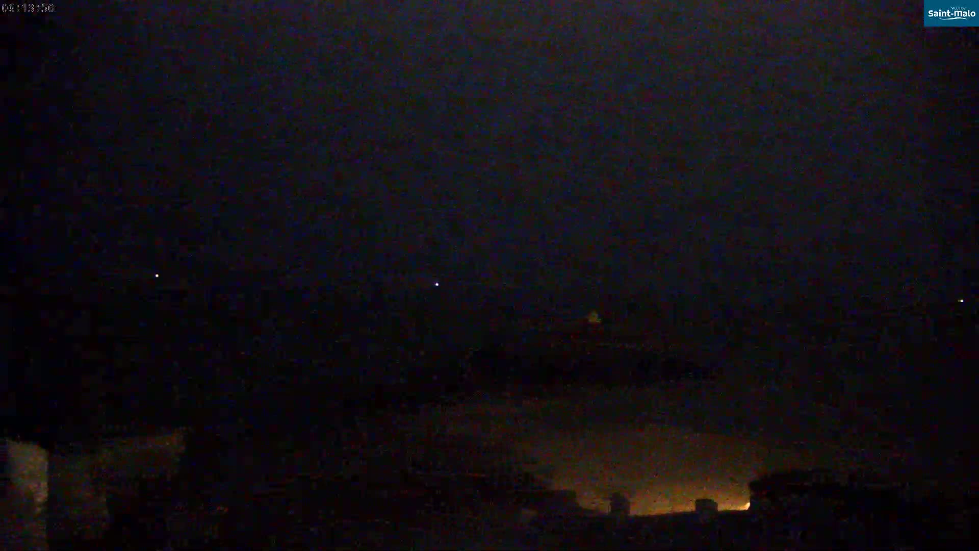 A nighttime, dark scene shows a few faint lights in the sky above a dimly lit, low horizon.