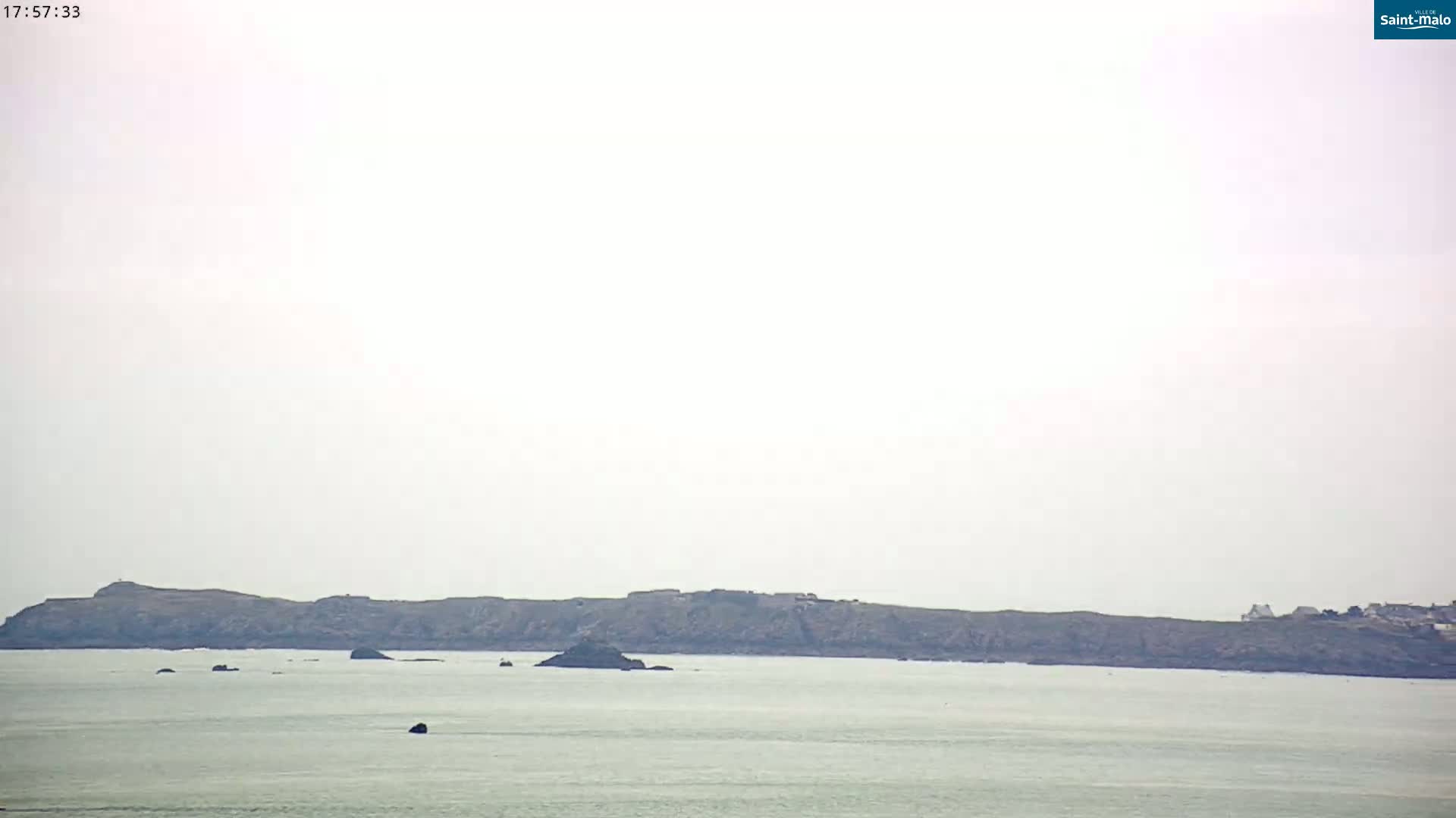 A hazy view shows a long, dark island in a calm body of water.
