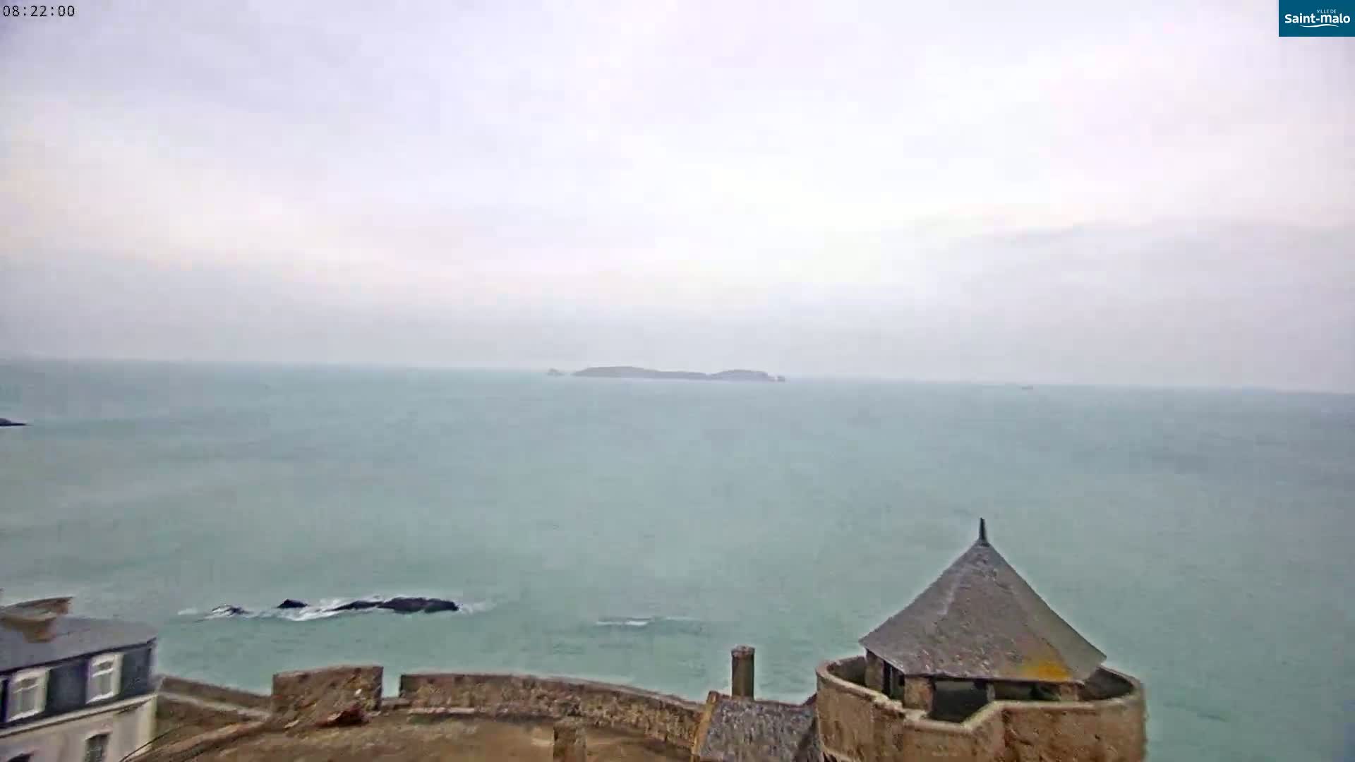 A coastal scene under an overcast sky shows a stone structure overlooking a calm sea with an island in the distance.