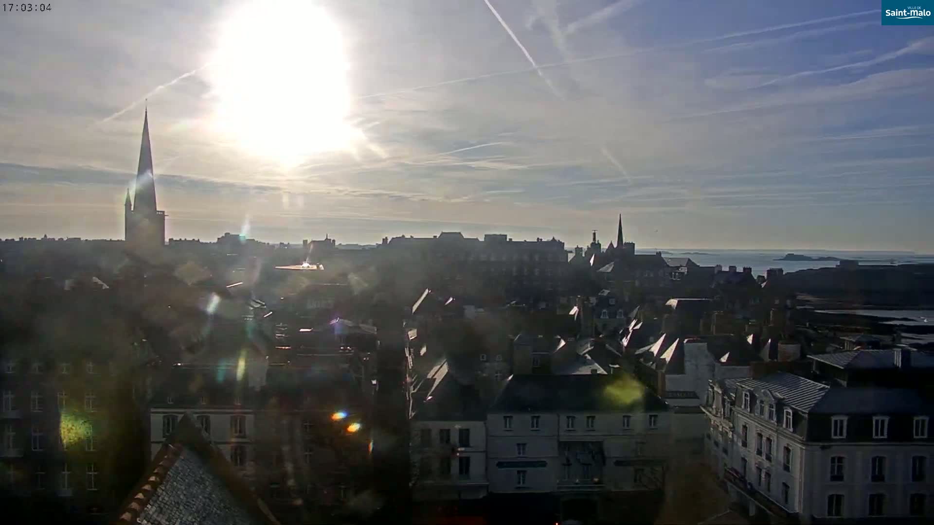 A sunny day reveals a cityscape with a tall church spire and ocean in the distance.