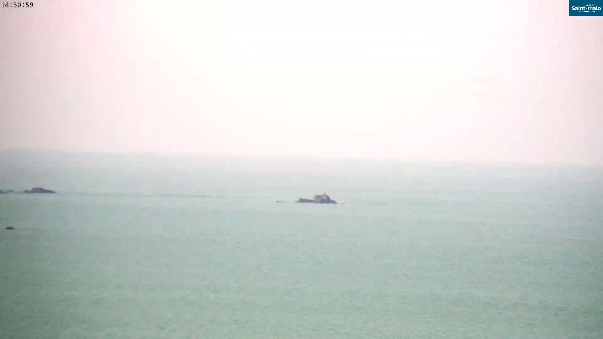 A hazy, light-green ocean with a few dark rocks and small islands visible in the distance.