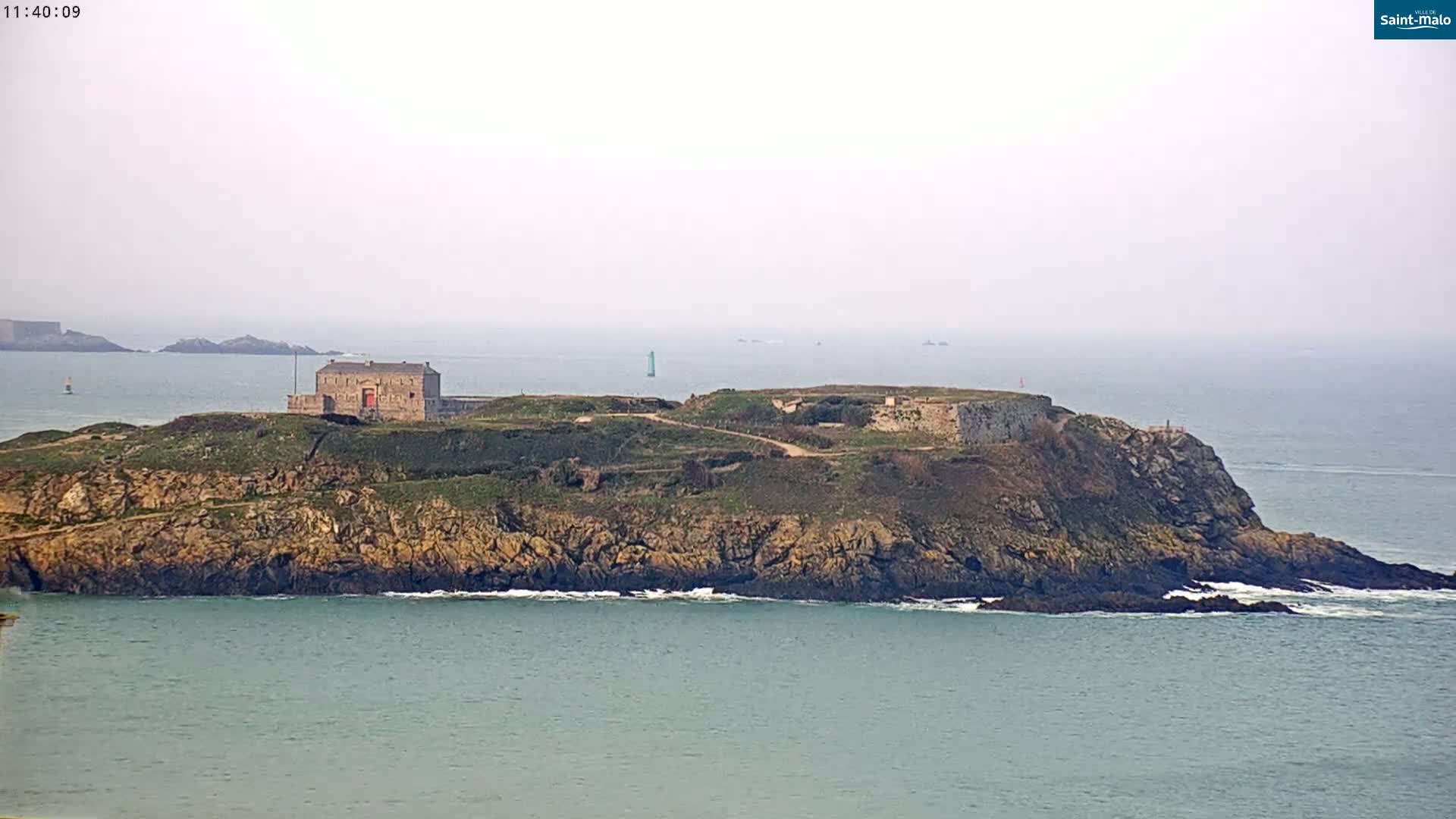A rocky island with a stone building and fortifications is visible in a hazy, calm ocean.