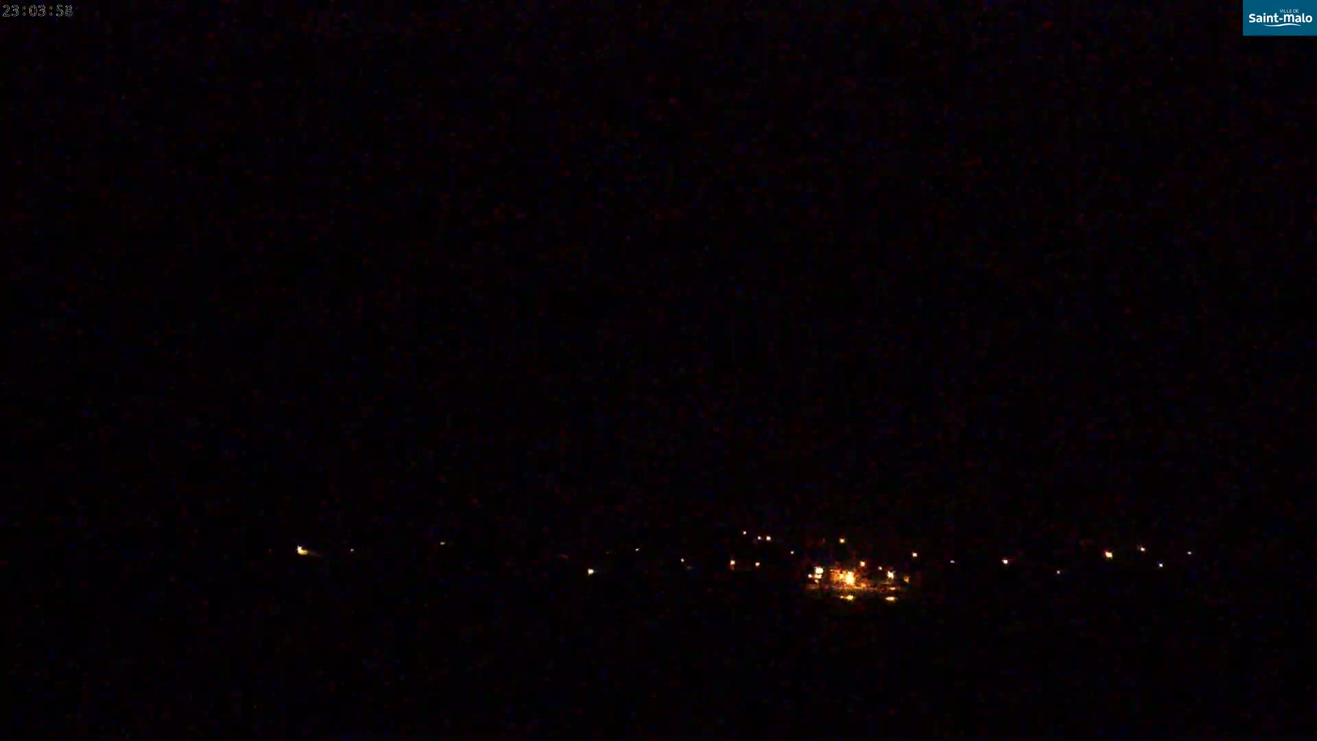 A dark, nighttime scene shows a line of faint, distant lights possibly from a town or village under a clear, black sky.