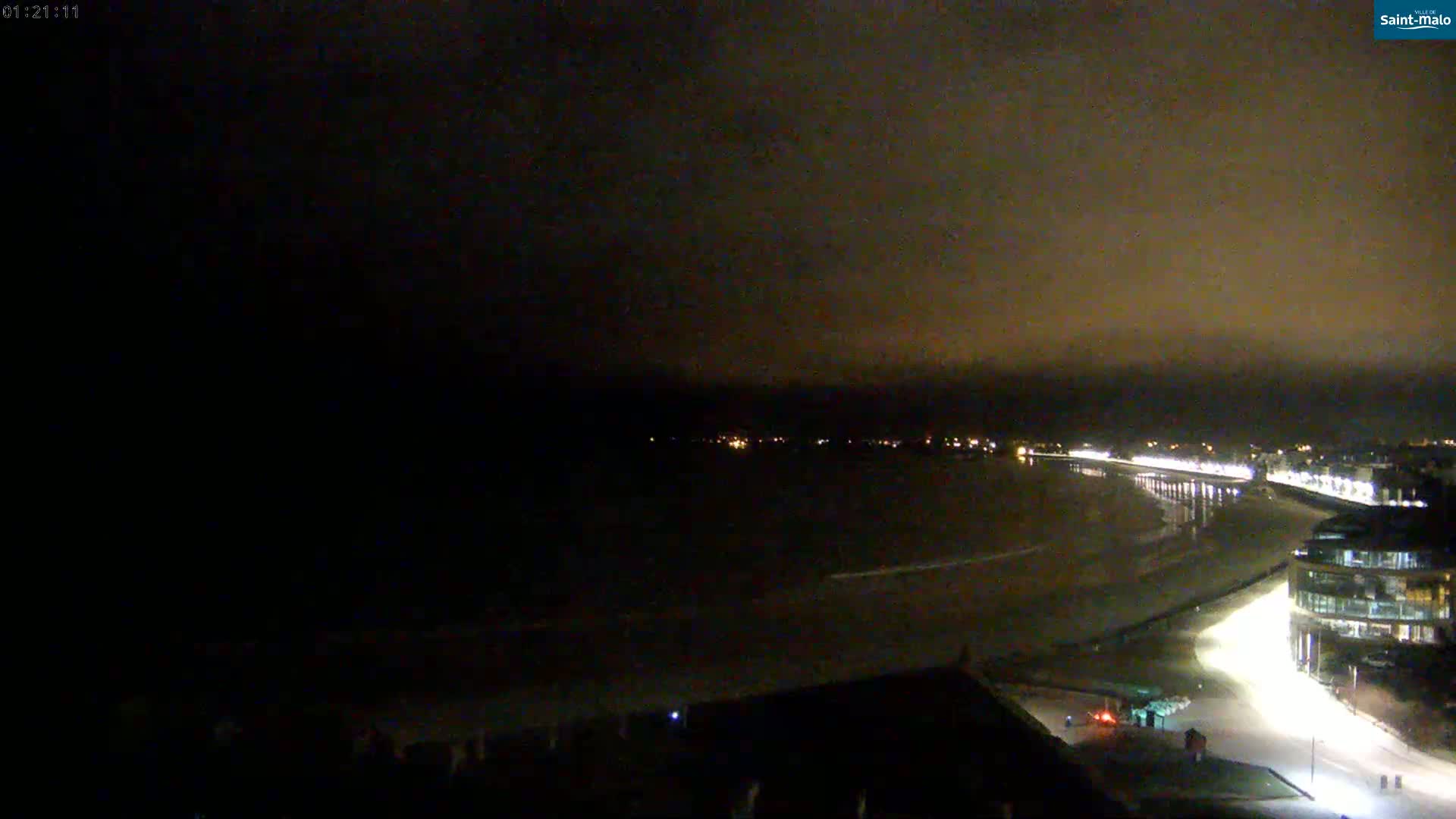 A nighttime view of a dimly lit beach and coastline, under a dark, cloudy sky.