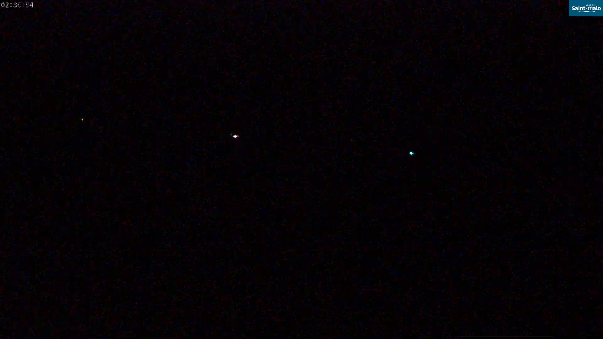 A dark nighttime scene shows three small, differently colored lights in the distance.