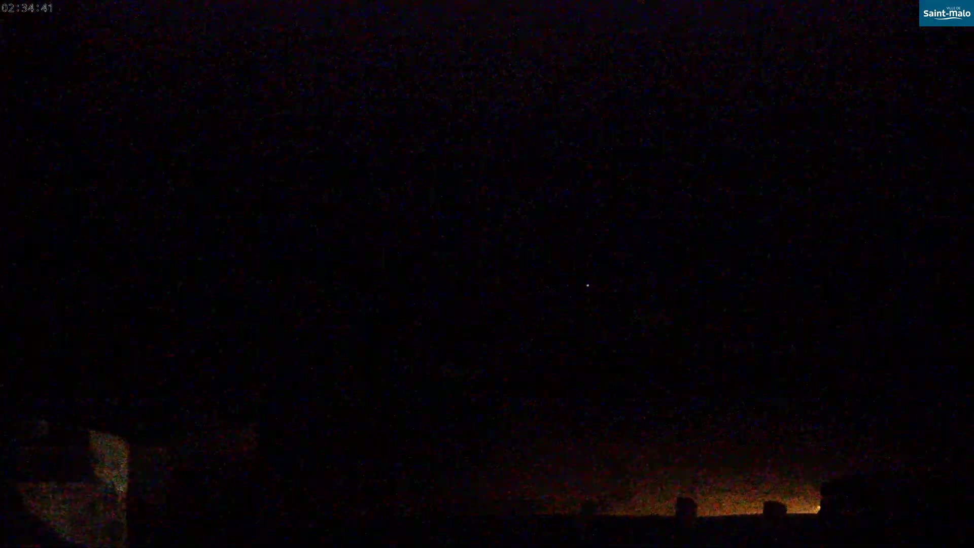 A nighttime view shows a dark sky with a single bright star and a faint orange glow on the horizon above a dark silhouette of rooftops.