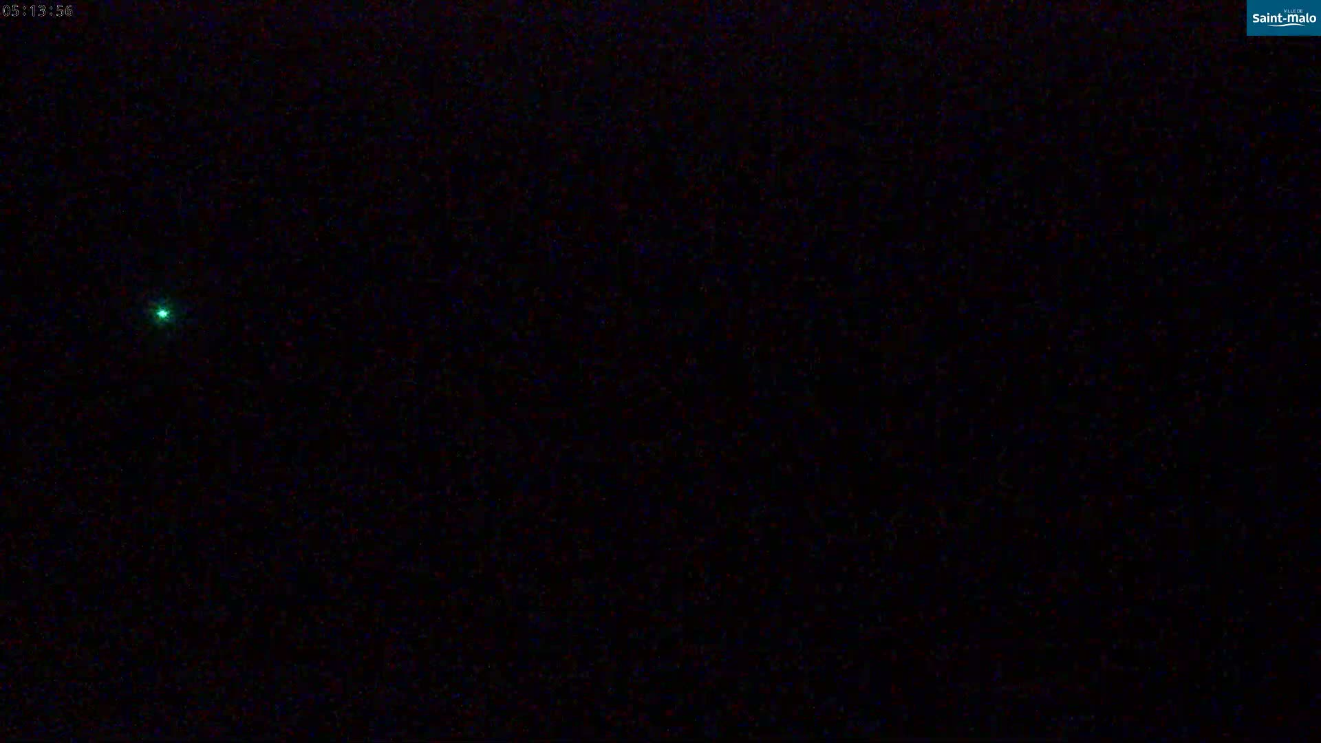 A small, bright green light is visible against a completely dark, nighttime sky.