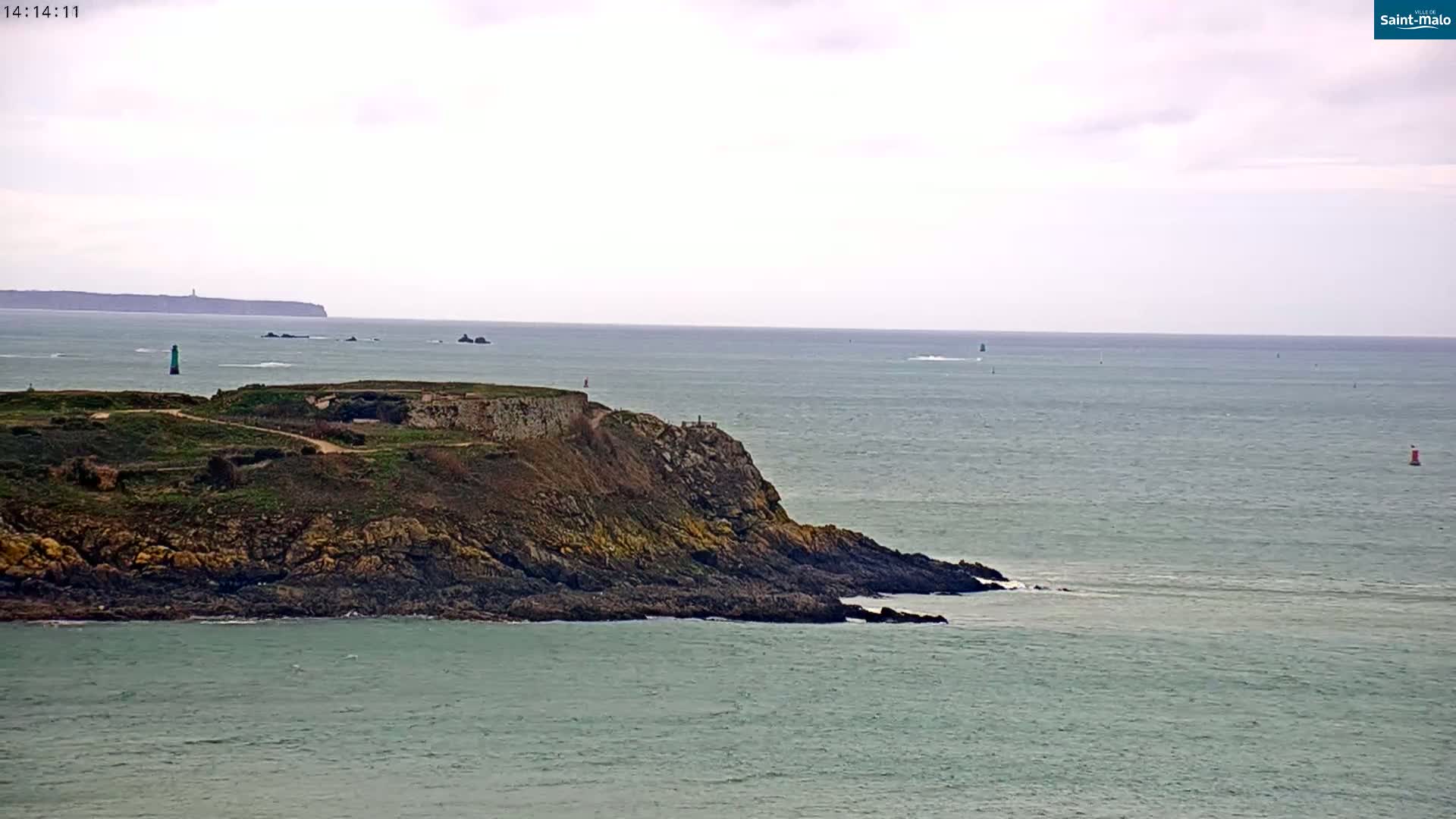 A rocky coastal headland juts into a calm, gray-green sea under an overcast sky, with a distant landmass visible on the horizon.