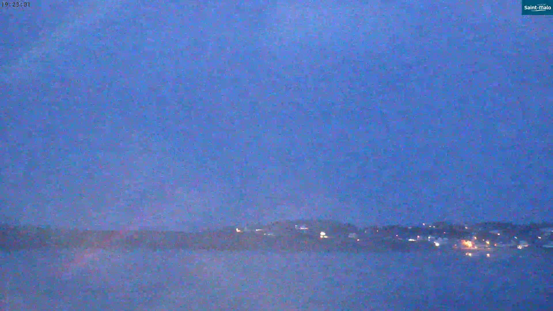 A blurry, low-light image shows a dark-blue twilight sky over a distant, faintly lit shoreline.