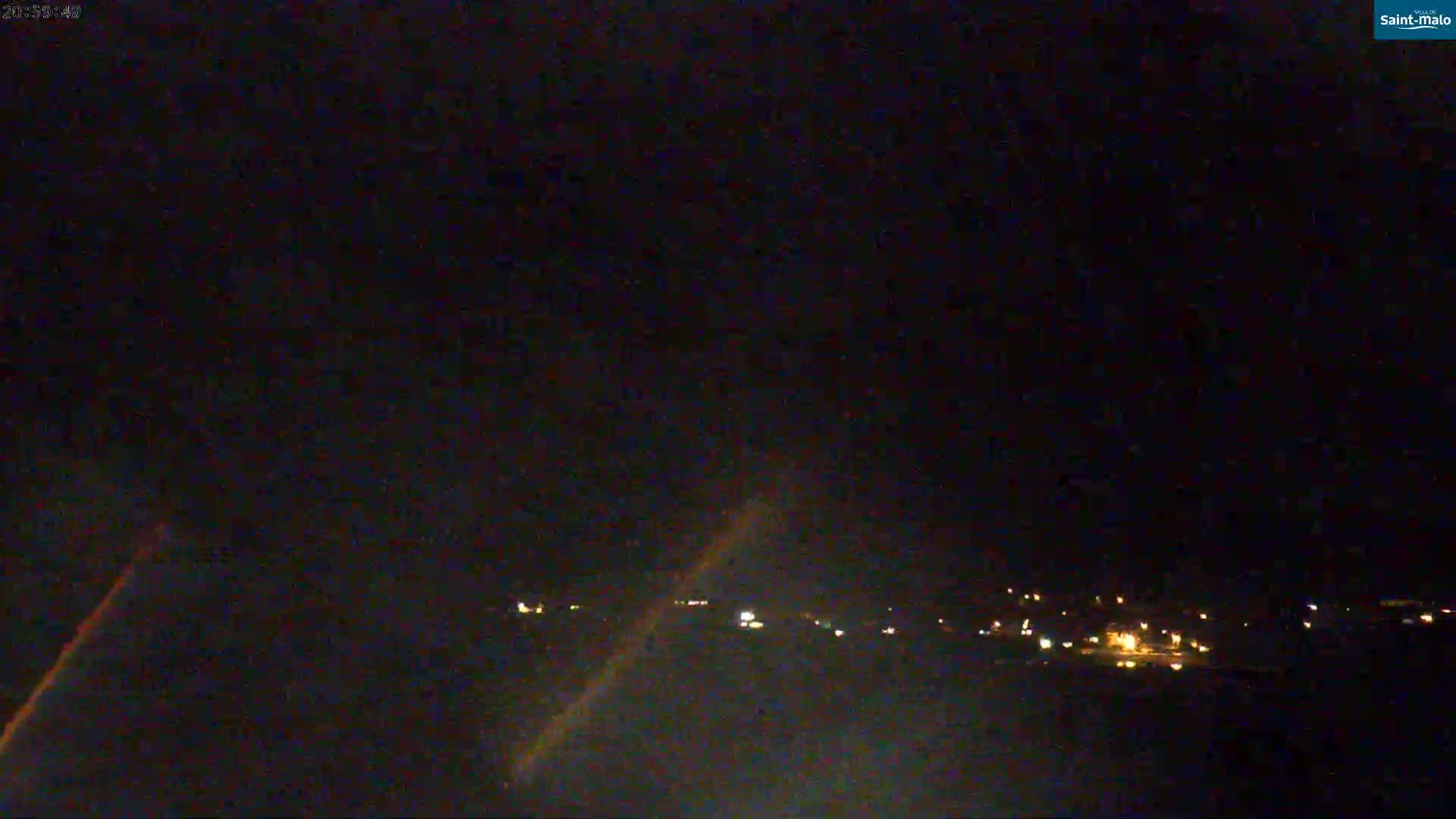 A nighttime, long shot shows a dark landscape with a few distant lights and a clear, dark sky.