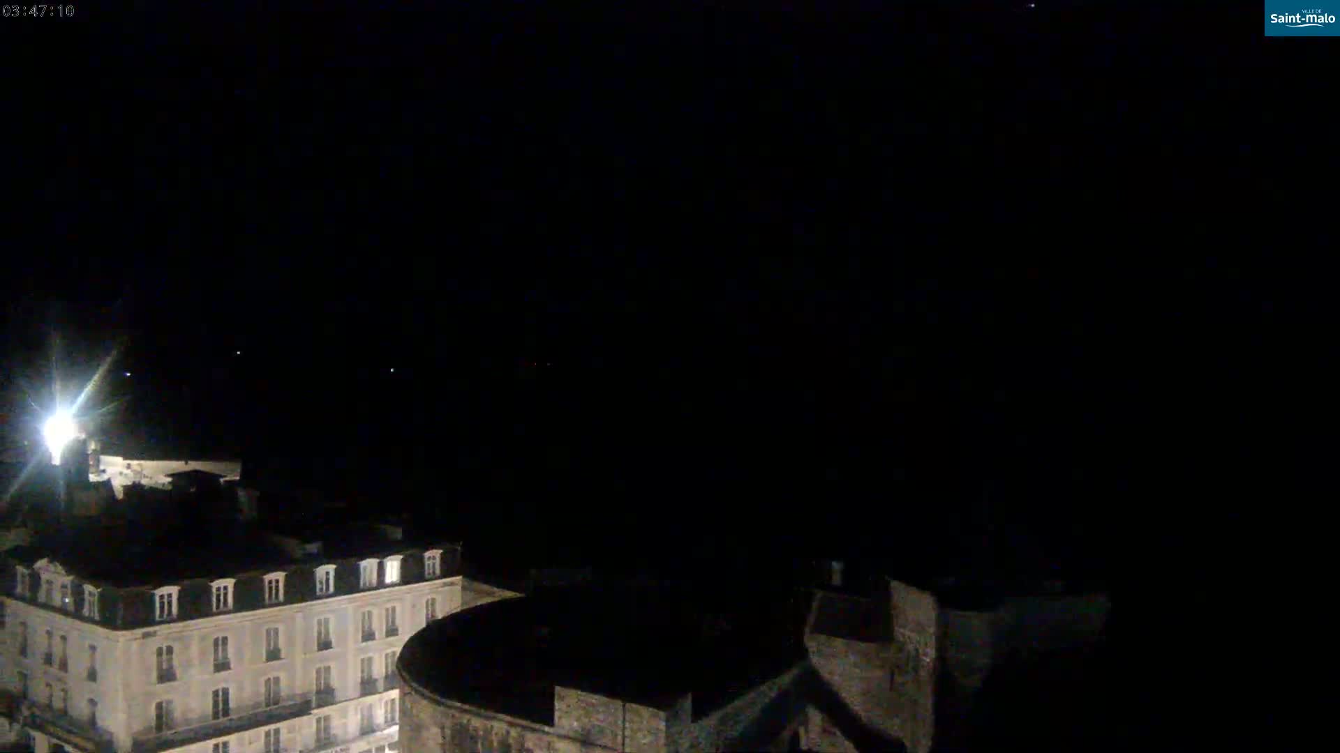 A nighttime view shows a city building and a stone wall under a clear, dark sky.