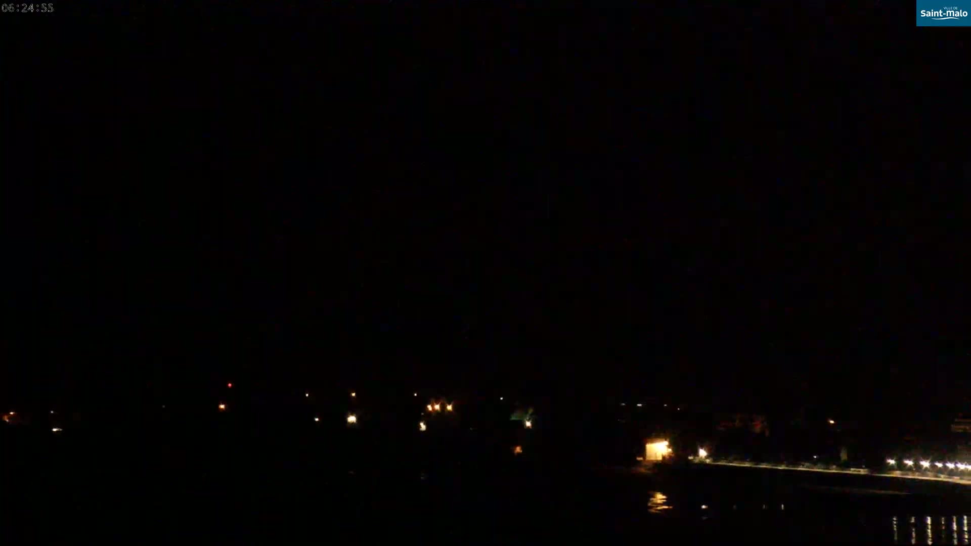 A nighttime view of a dark shoreline with scattered lights and a body of dark water.