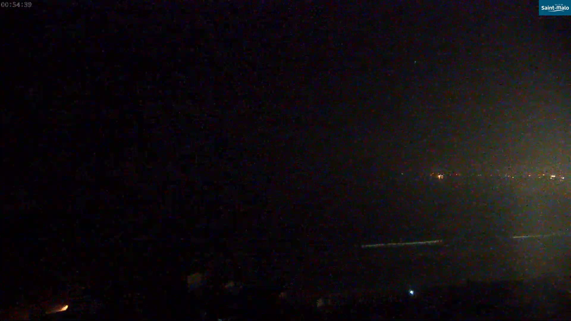 A dark, nighttime scene shows a distant line of lights on the horizon under a clear, starlit sky.